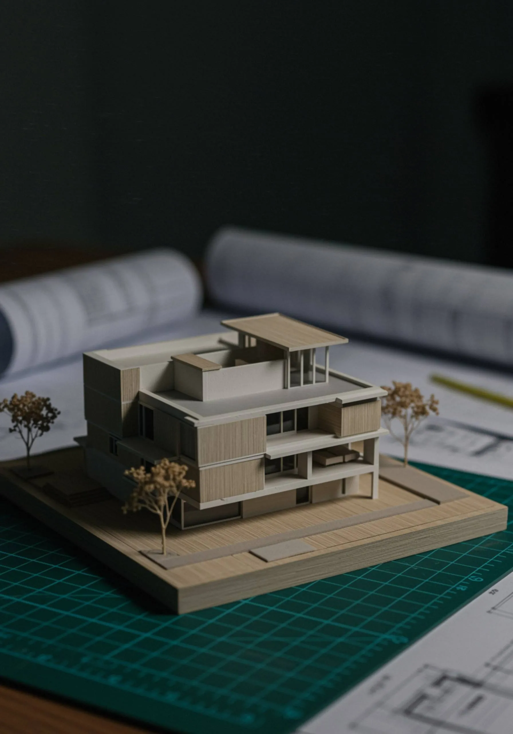 "Modelo arquitectónico 3D detallado de un proyecto residencial en una mesa, rodeado de hojas de planos y una base de corte, con iluminación suave y alta claridad."